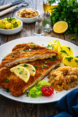Crispy breaded fried cutlet with boiled potatoes and cooked cabbage on wooden table

