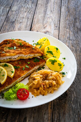 Crispy breaded fried cutlet with boiled potatoes and cooked cabbage on wooden table
