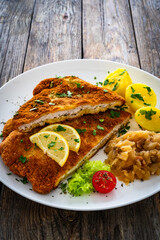 Crispy breaded fried cutlet with boiled potatoes and cooked cabbage on wooden table
