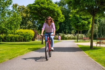 Beautiful mid adult woman riding bicycle in city park
