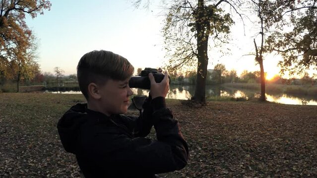 Young caucasian guy boy teen photographer takes pictures in the evening autumn park among the trees
