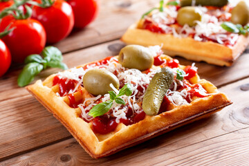 Appetizing pizza waffle with vegetables tomatoes, cucumber, olives, sausages, cheese and herbs on a board