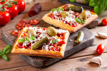 Pizza waffle toast with tomatoes, sausages, cheese and herbs on a board