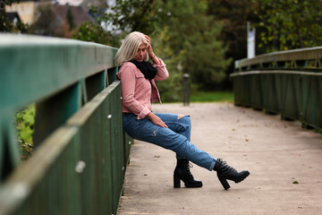 Woman blonde in her fifties with a pink denim jacket, blue jeans with a ripped black sweater and a...
