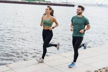 Active couple running by the river, enjoying fitness together in an urban environment.