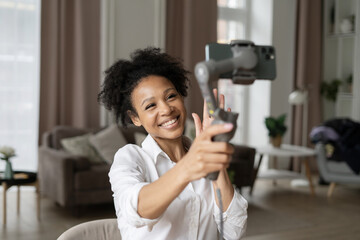 Joyful vlogger giving a thumbs up while recording with a smartphone gimbal in a cozy living room.