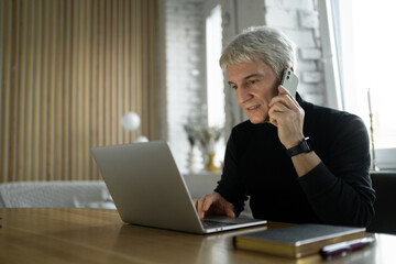 Focused senior professional multitasking with a laptop and phone in a stylish office setting.