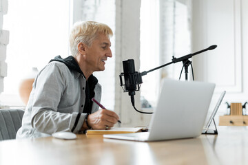 Podcaster recording a new episode, smiling as he speaks into a professional microphone, with laptop...