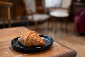 Croissant on wood table in blurred coffee shop background.