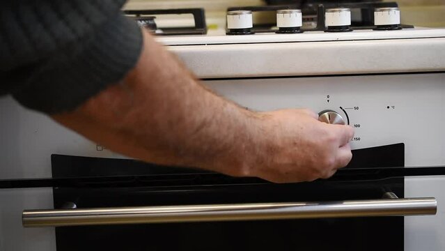 By turning the knobs on the gas stove panel, the man stops the oven from working.
