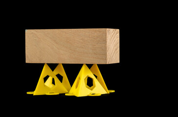 Wooden block supported on  yellow stackable painters display pyramid triangles isolated on a black...