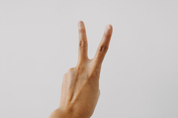 Photo of woman's tan skin hand showing numbers two, counting fingers gesture, isolated on white background wall.