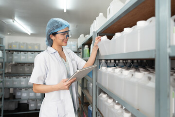 Asian female chemist checks products (solvent) on shelves with digital tablet.