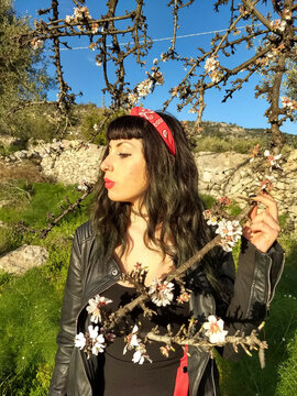 A sultry pin-up dons a black dress with red accents, posing gracefully beside a blossoming almond tree branch.