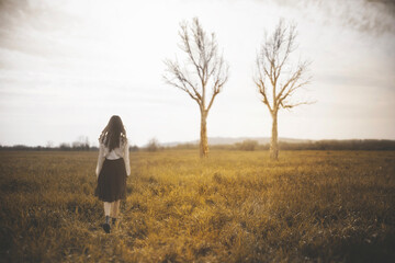 woman walking towards two trees on the horizon that seem like a door to the infinite