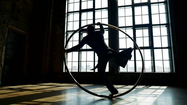 enigmatic man in black overcoat whirling on hoop in dancehall, silhouette against window