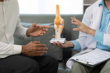 Male doctor and male patient discussing knee joint model It is likely that the focus will be on the...