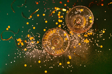 Two exquisite glasses of champagne with silver glitters and confetti. Stylish alcohol cocktail on green background with gold serpentine and glitters.