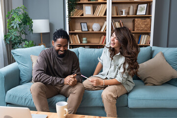 Young married couple two people looking forward to positive pregnancy test they planned to become parents and start family. Happy man and pregnant woman hugging while sitting on the sofa in their home