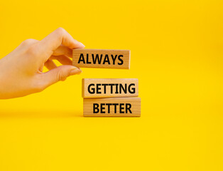 Always getting better symbol. Wooden blocks with words Always getting better. Beautiful yellow background. Businessman hand. Business and Always getting better concept. Copy space.