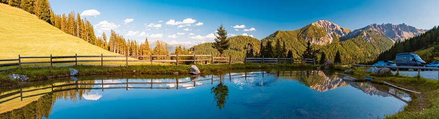High resolution stitched alpine summer panorama with reflections in a pond at the famous Maria...