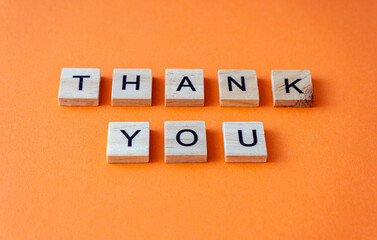 Thank you word. The phrase is laid out in wooden letters top view. Orange flat lay background