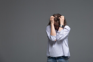 A woman covered her face with her hands in fear on a gray background.