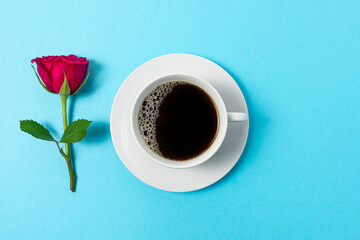 Creative composition of red rose flower and cup of coffee on blue background. Minimal spring concept.