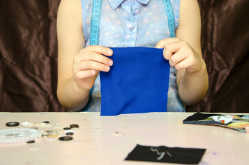 Fototapeta na wymiar Hands of a little needlewoman , a child in a blue blouse chooses pugawicki and fabric and then sews. 