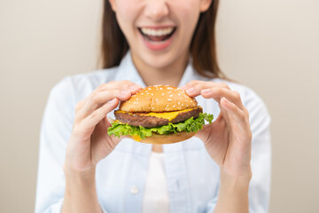 Fast Food concept, happy delicious asian young woman eating tasty burger or hamburger with cheeseburger, girl hungry holding junk food with meat and vegetable in brunch, lunch. Unhealthy snack meal.