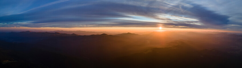 Aerial view of dark mountain hills with bright sunrays of setting sun at sunset. Hazy peaks and...