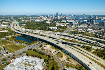 Obraz premium Aerial view of Jacksonville city with high office buildings and american freeway intersection with fast moving cars and trucks. USA transportation infrastructure concept