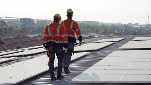 A technician sits on a rooftop, examining solar panels under a clear blue sky. He points while taking notes, ensuring everything is functioning properly.