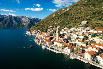 Motor boats are moored off the coast of Perast opposite the bell tower of the Church of St....