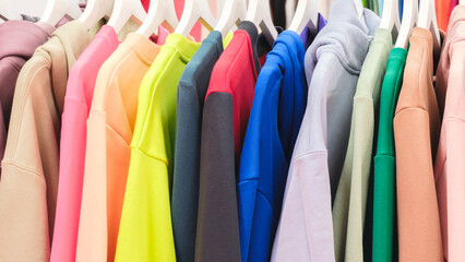 Multi-colored clothes on hangers in the store, fashion clothing concept background