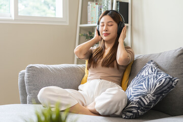 Pretty relaxing, happy asian young woman, girl listening to music, enjoy song or watching videos, podcast on mobile with white wireless headphones sitting on sofa, couch at home, chill out and leisure