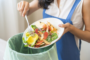 Compost from leftover food asian young housekeeper woman, female hand holding salad bowl use fork scraping waste, rotten vegetable throwing away into garbage, trash or bin. Environmentally responsible