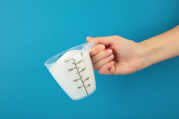 Measuring spoon with washing powder in hand on blue background