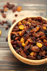 Dry raisins in wooden bowl on brown wooden background. Vertical photo