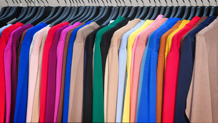 Multi-colored clothes on hangers in the store, fashion clothing concept background