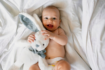 Little newborn baby boy smiling, have fun with bunny toy at home in bed