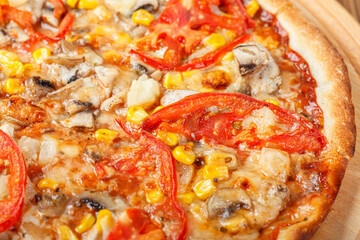 delicious pizza with chicken, mushrooms, cheese, tomatoes and corn on a wooden background