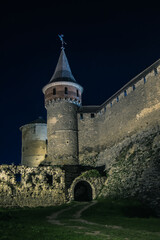 Fototapeta premium View of the towers and walls of the Kamianets-Podilskyi Castle in the night. Stone bastion of an ancient castle. Beautiful stone castle on the hill at night. Ukraine