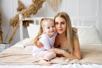 mom and daughter play, hug and kiss at home on the bed, lifestyle, tender relationship of a young mother and child, happy family and motherhood