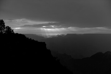 Evening sunbeams streaming through the clouds creates a dramatic black and white photo of silhouetted ridgelines in Grand Canyon National Park after a stormy August day in Arizona, USA.