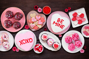 Valentines Day table scene with a variety of fun desserts and sweets. Top down view on a dark wood...