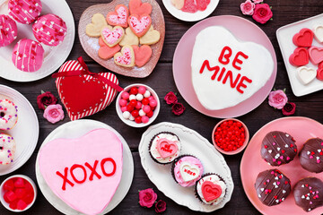 Valentines Day table scene with a selection of fun desserts and sweets. Above view on a dark wood...