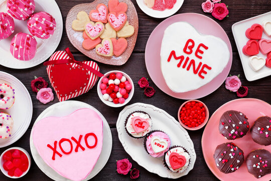 Valentines Day table scene with a selection of fun desserts and sweets. Above view on a dark wood background. Love and hearts theme.