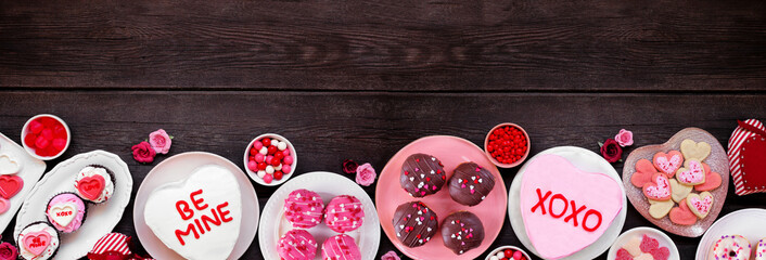 Valentines Day bottom border with a variety of fun desserts and sweets. Top down view on a dark...