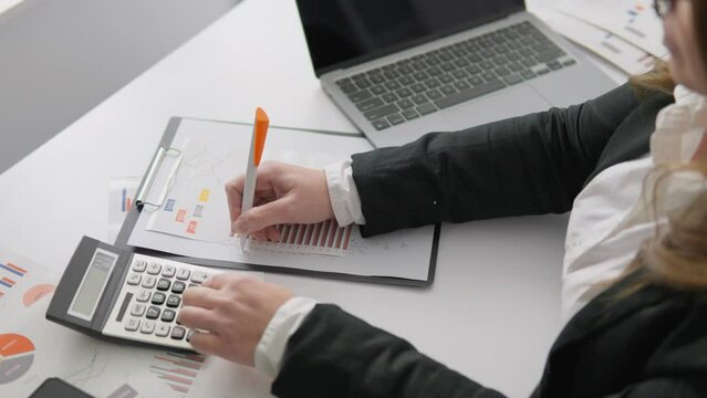 A financial analyst keeps records and analyzes data in the workplace using modern technology and a calculator. A female accountant works intently on preparing financial reports and making calculations